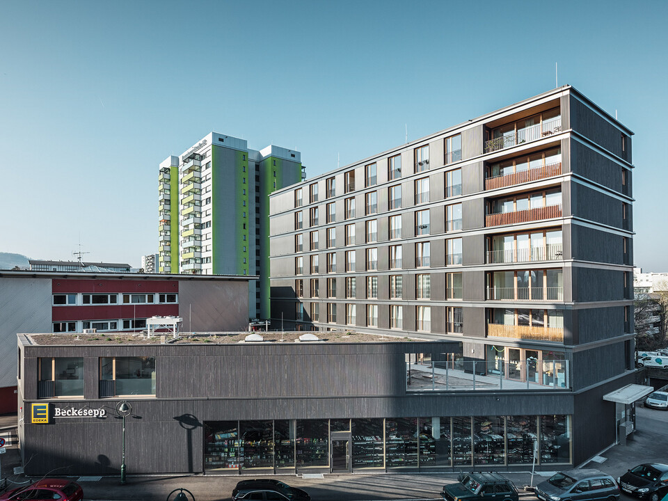 Street view of the black grey multifunctional building Buggi 52 with its built environment.