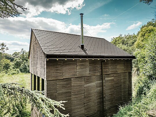 Hinteransicht eines Hauses mit PREFA Dachschindeln in P.10 Nussbraun mit PREFA Entwässerungssystem, umgeben von natürlichem Gelände im Westen Frankreichs
