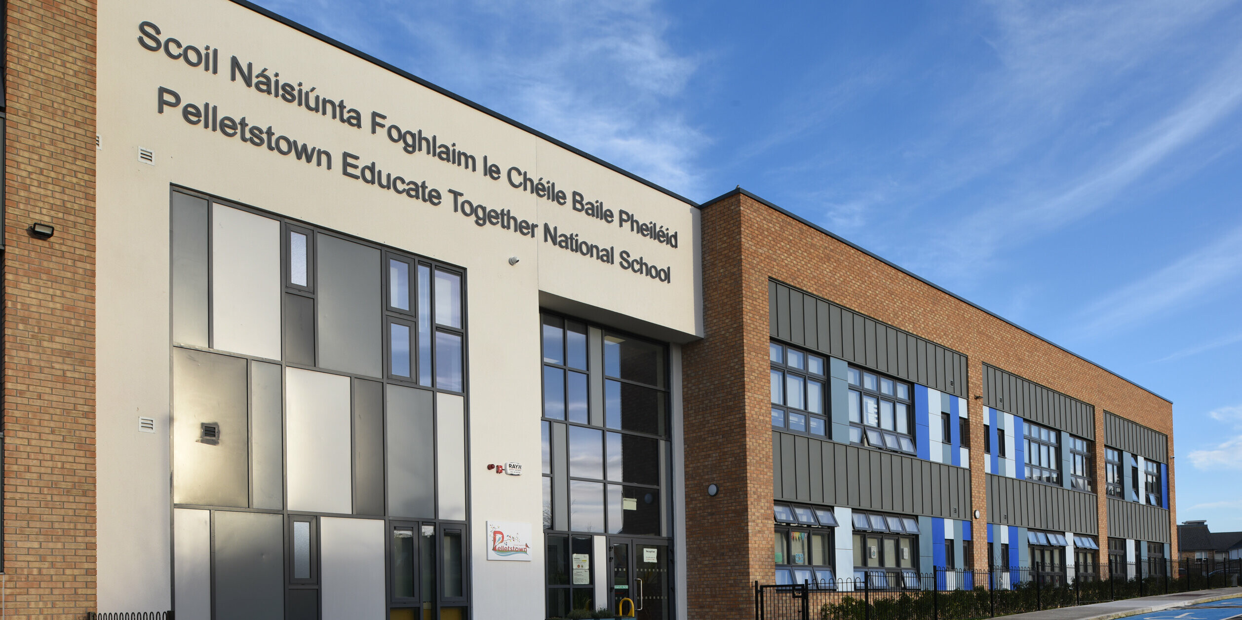 Entrance to Pelletstown Educate Together National School in Dublin. The façade of the school is an exciting material mix of aluminium, plaster and traditional brick. The PREFALZ standing seam cladding in P.10 light grey underlines the modern and sustainable architecture. Bicycles in front of the entrance demonstrate the school's commitment to sustainability. Shrubs under the rows of windows add visual interest to the robust building materials.