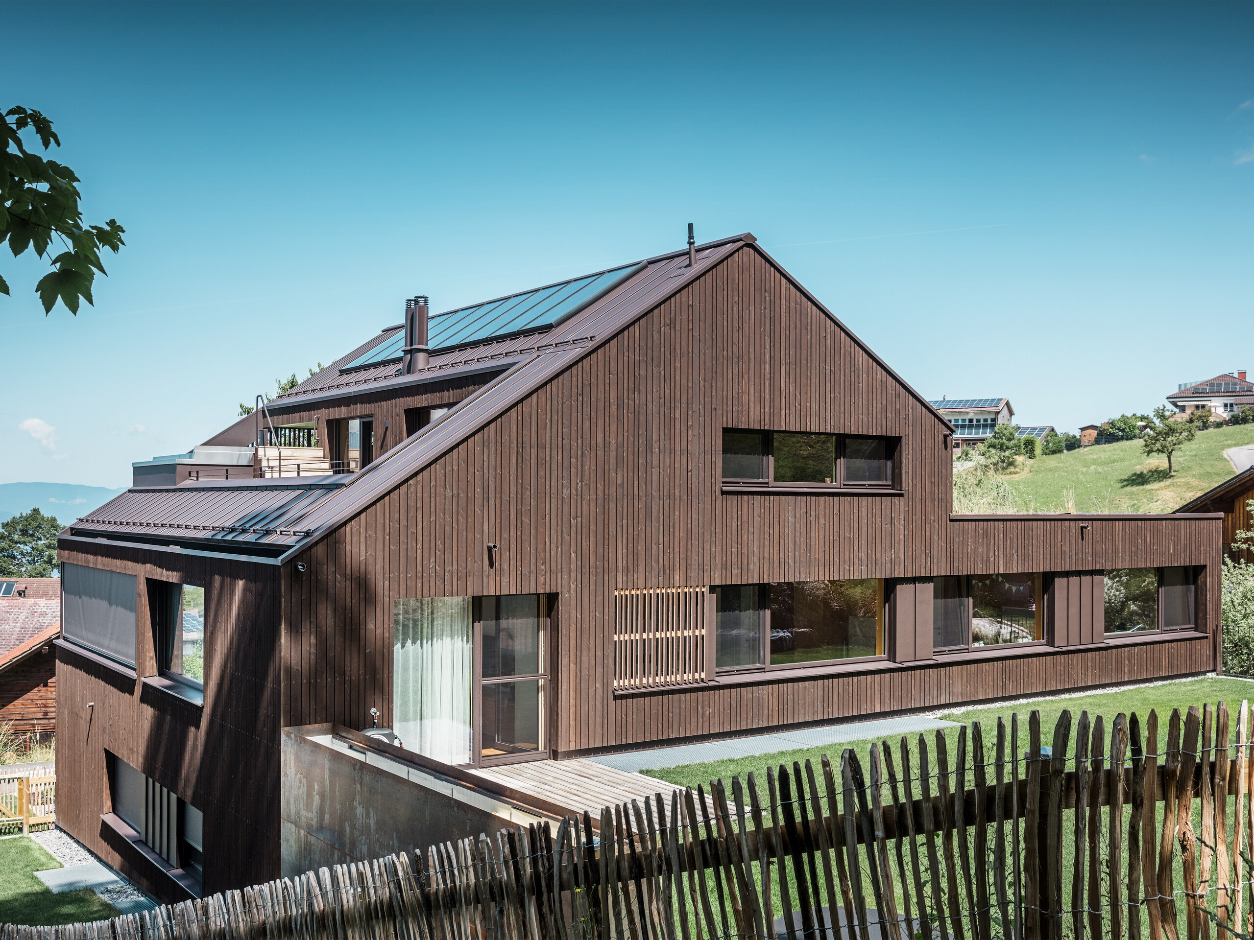  The monochrome multi-family house with the aluminium roof and the silver fir façade from a lateral perspective after the conversion.