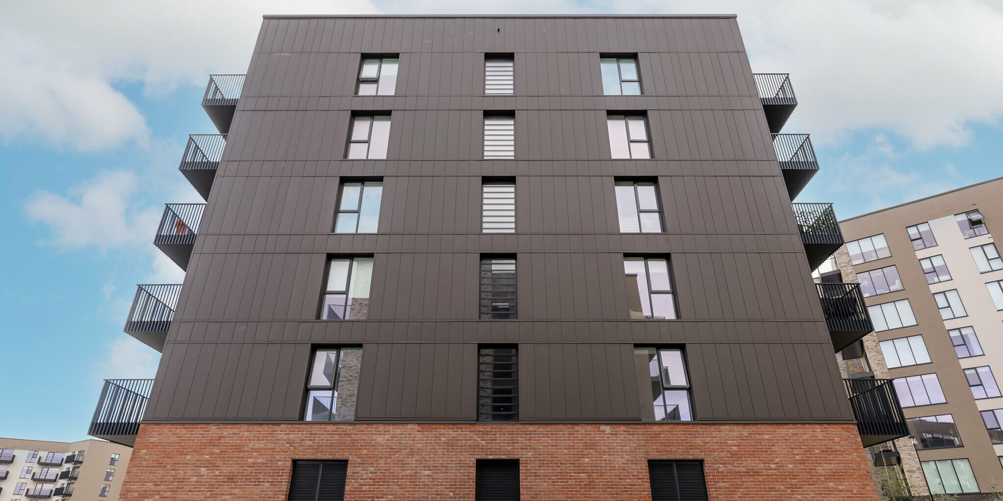 A frog's-eye view of the Citywest Apartments in Dublin. The 700 m² of vertically laid PREFA sidings in P.10 brown combine with the brick façade to form a harmonious and durable unit. The modern aluminium panels from PREFA ensure sustainability and design.