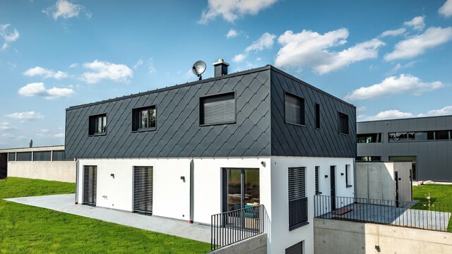 Modest new build with flat roof; the ground floor has a white plaster finish while the upper floor is clad in the large PREFA rhomboid façade tile in anthracite.