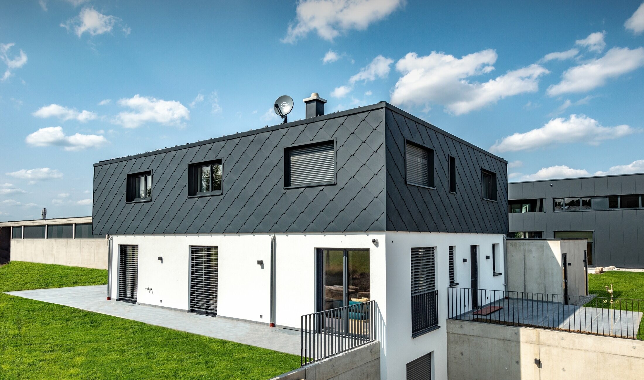 Modest new build with flat roof; the ground floor has a white plaster finish while the upper floor is clad in the large PREFA rhomboid façade tile in anthracite.