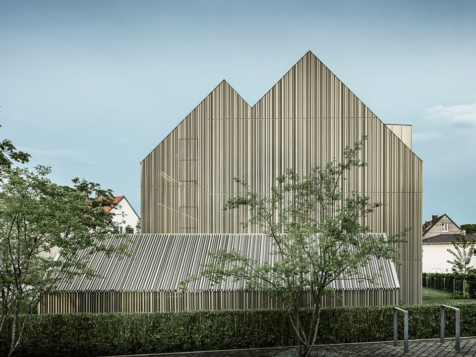 The residential building in Dachau realised by the office lynx architecture from a normal perspective from the side, surrounded by green areas, trees and neighbouring buildings.