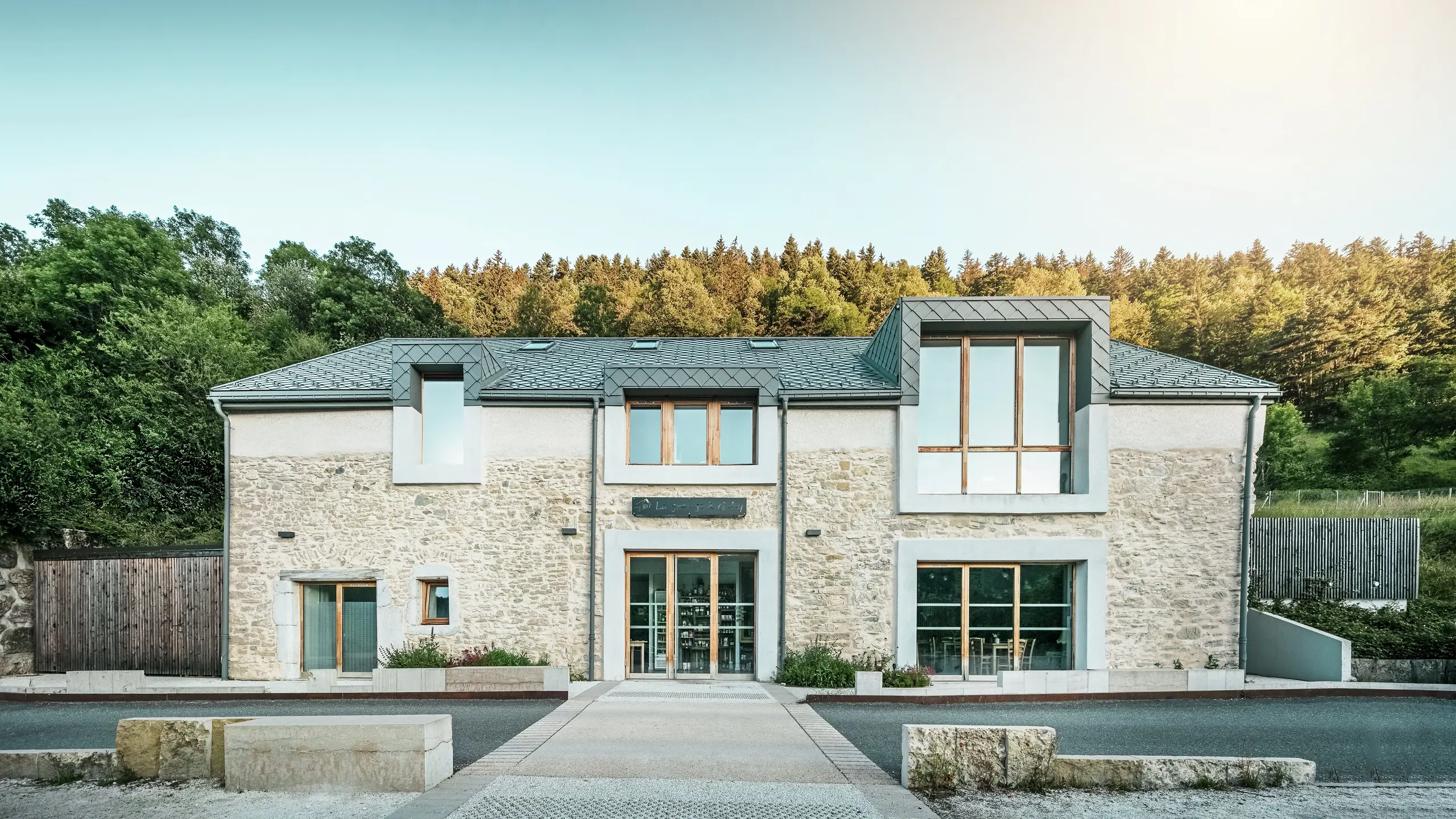 Front view of the restored barn ‘La Grange à Gaby’ in Engins, France. The combination of traditional stone masonry and a modern PREFA aluminium roof with 29 × 29 cm rhomboid tiles gives the building a harmonious and contemporary look. Today, the barn serves as a cultural meeting place and hostel.