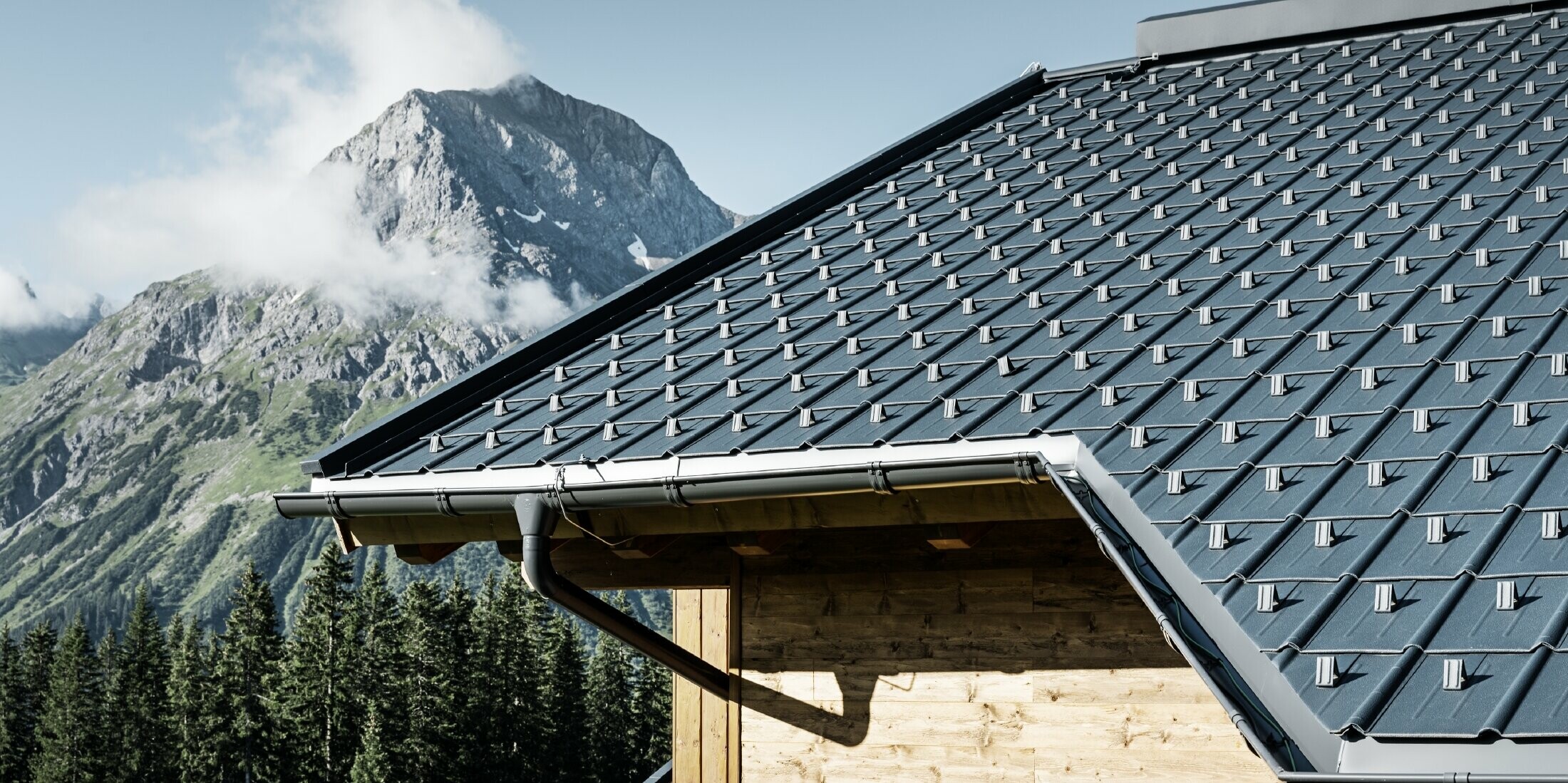 Wooden house in the mountains, the roof is covered with PREFA roof tiles in anthracite with a PREFA gutter and wooden façade