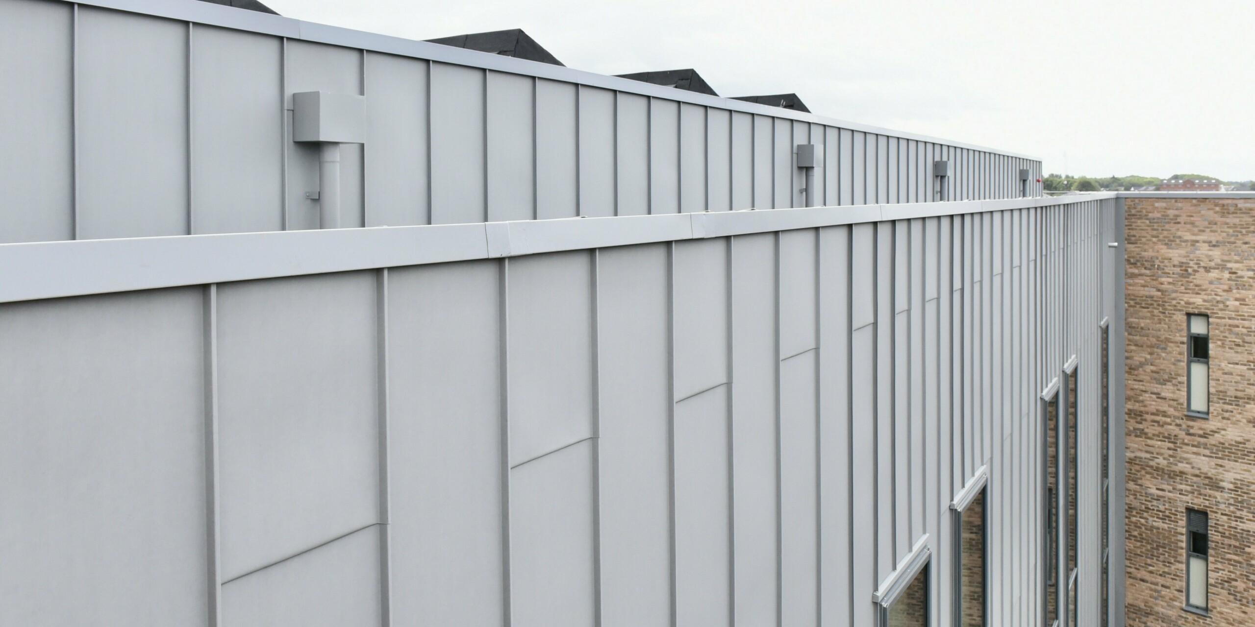 Detailed view of the PREFALZ (standing seam) aluminium facade in patina grey at the Regional College North, UK. The clear lines and matt appearance of the standing seam cladding emphasise the high-quality workmanship and timeless design.
