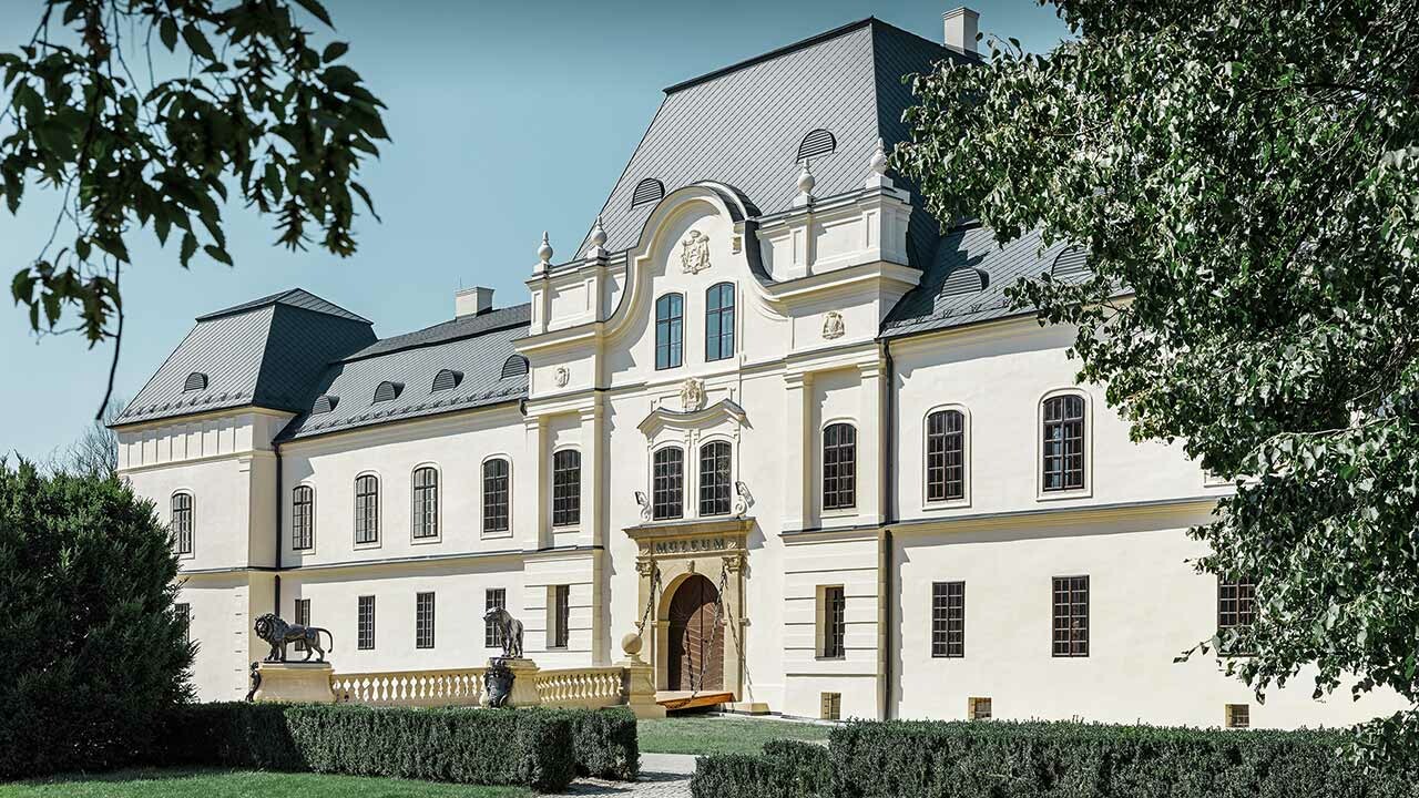 Side view of Humenné castle with trees in the foreground, roof renovation with the PREFA roof tiles in anthracite