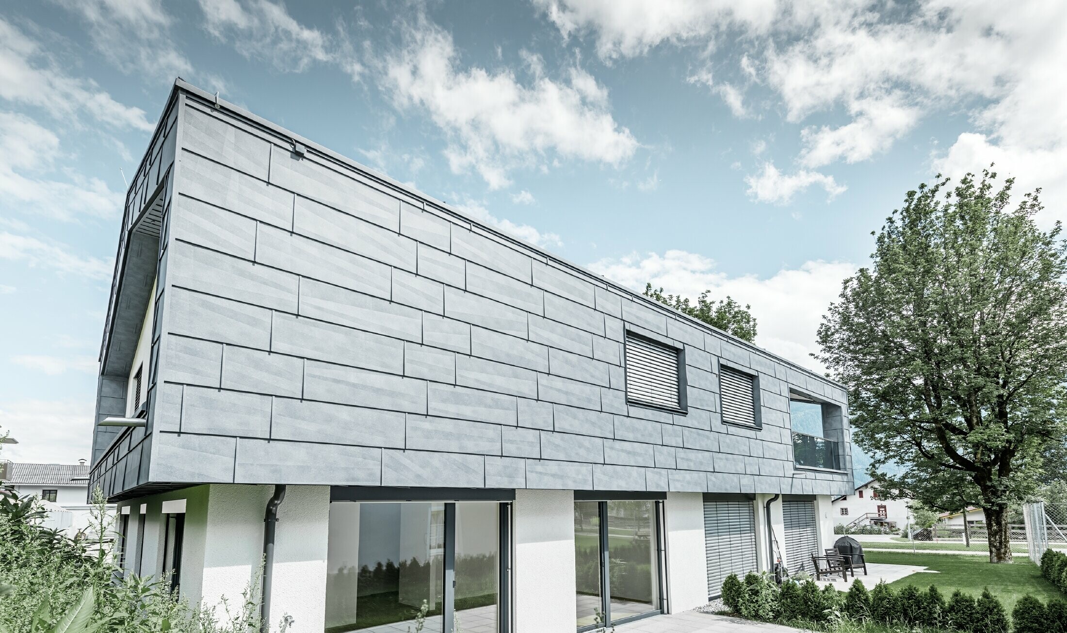 Modern detached house with gabled roof without soffit; the top floor was clad in the PREFA façade panel in stone grey.