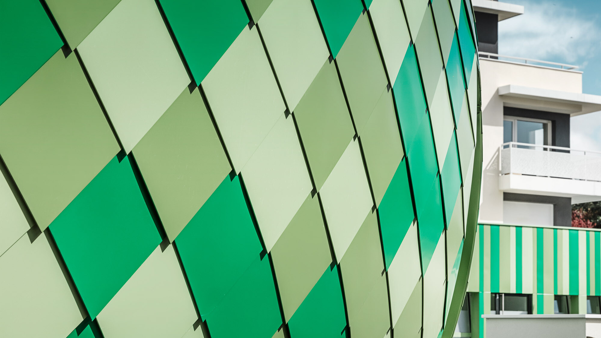 Close-up of the aluminium cladding made of rhomboid tiles in the bespoke colours grey-green, reseda green and mint green from the side. 