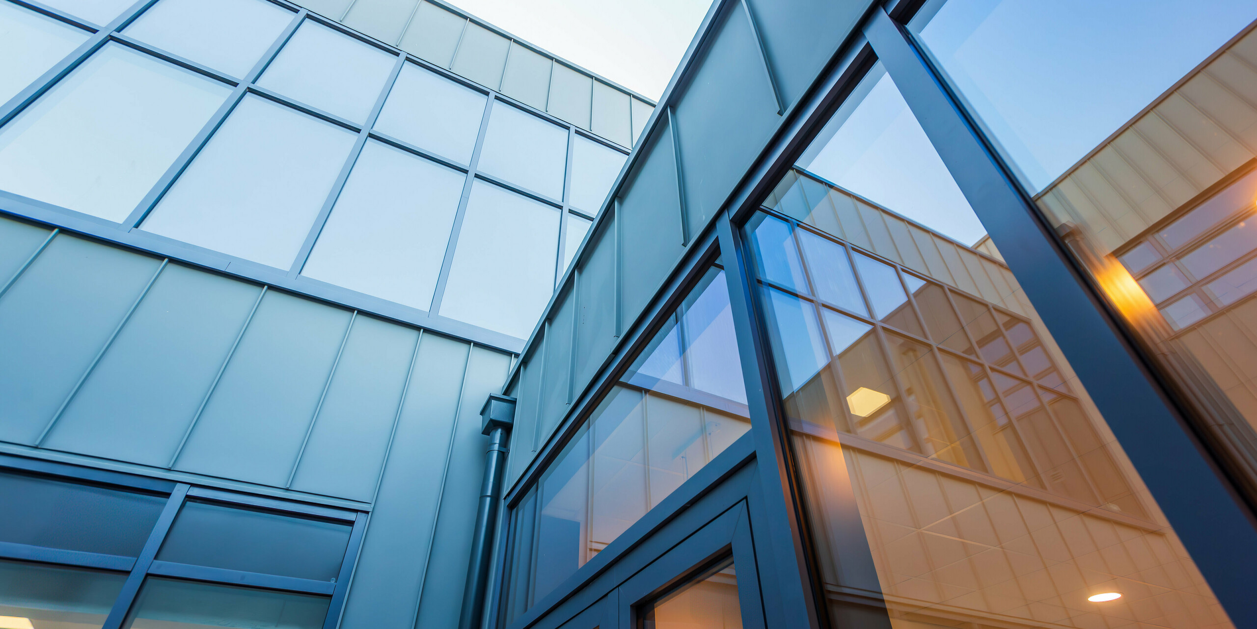 A worm's eye view of the modern PREFALZ aluminium facade in P.10 light grey of Scoil Mhuire Naofa in Carrigtwohill, Republic of Ireland. Large window areas and precise standing seam tracks emphasise the contemporary architecture and ensure a light-flooded, elegant design.