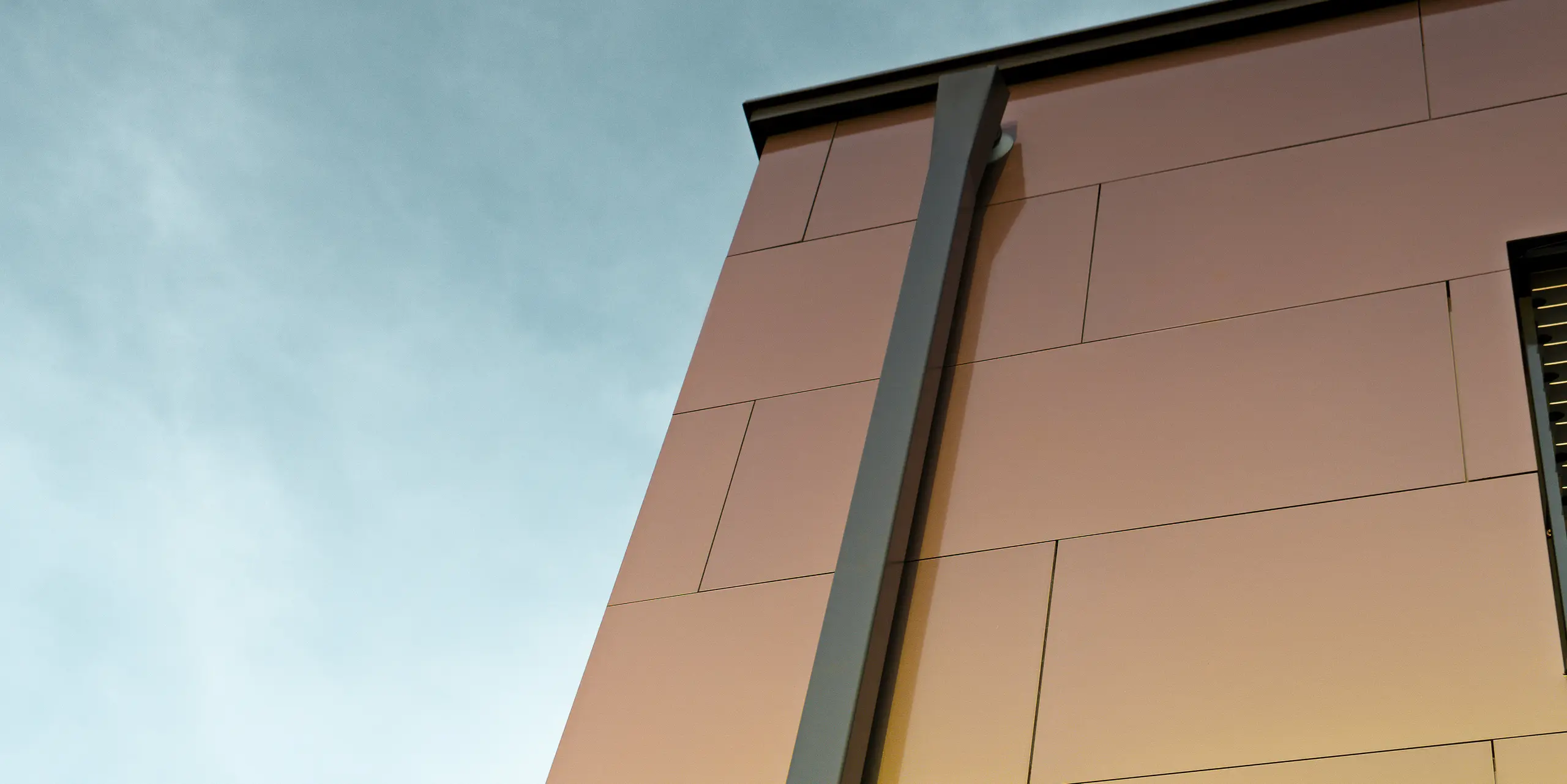 Side of a modern detached house with the modern PREFA square downpipe for draining the flat roof. The façade is clad with aluminium composite panels in the iridescent colour ‘spring lake’.