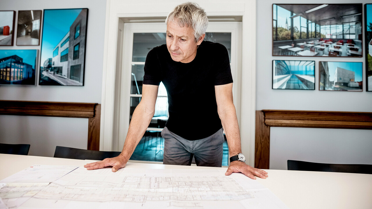 An architect is working on detailed building plans in a modern office, surrounded by impressive photos of PREFA architectural projects.