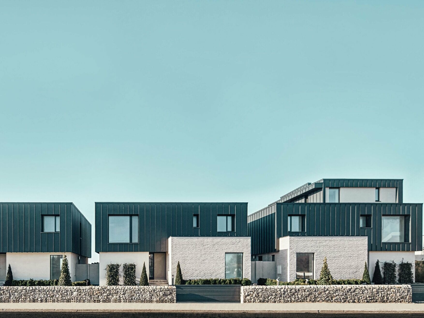 Front view of the terraced houses with flat roof on a sunny day. The façade of the upper floor is covered in Prefalz P.10 anthracite.