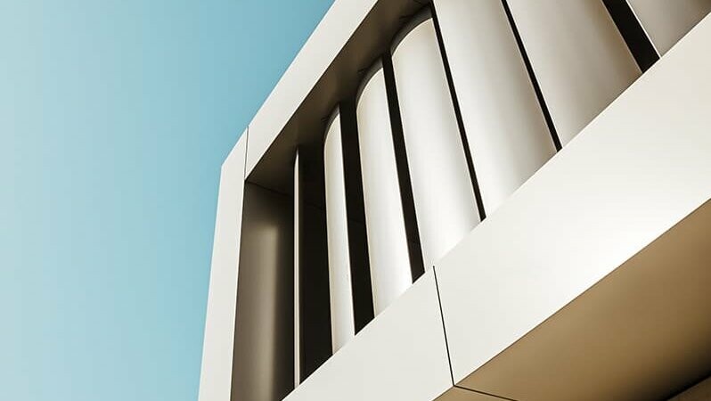 Diagonal view of the left edge of the façade from the right below, from bottom to top: stone façade, aluminium façade with slats