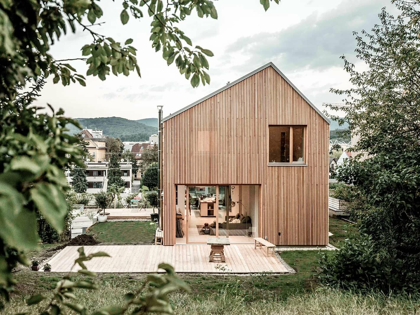 A photo from the terrace of the house. The wooden style is used to its fullest, in combination with the trees it looks very natural. Through the large terrace window, the view falls into the open living room.