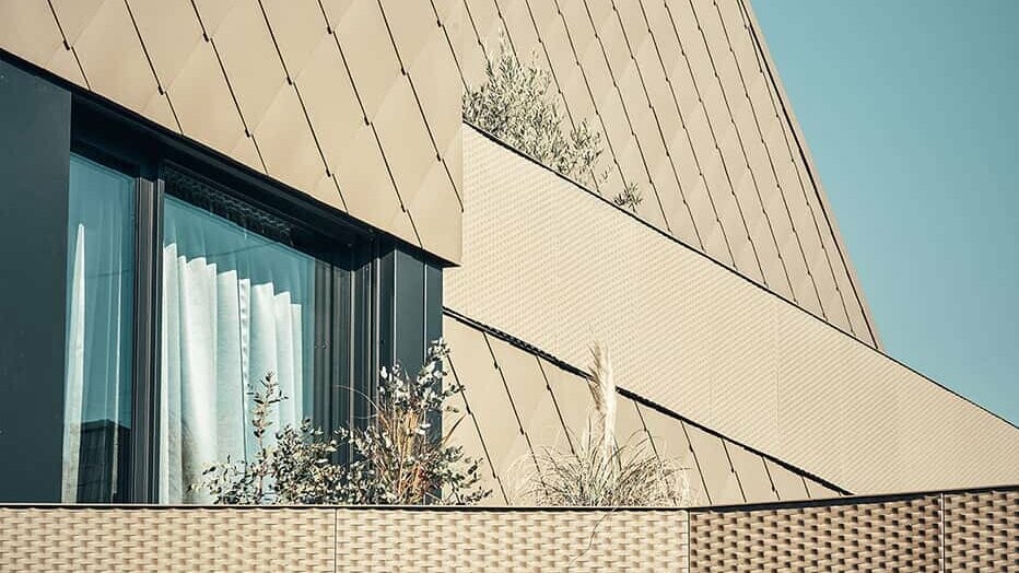 The illustration shows a section of PREFA rhomboid façade panels 44 x 44 in the special coating P.10 Bronze.