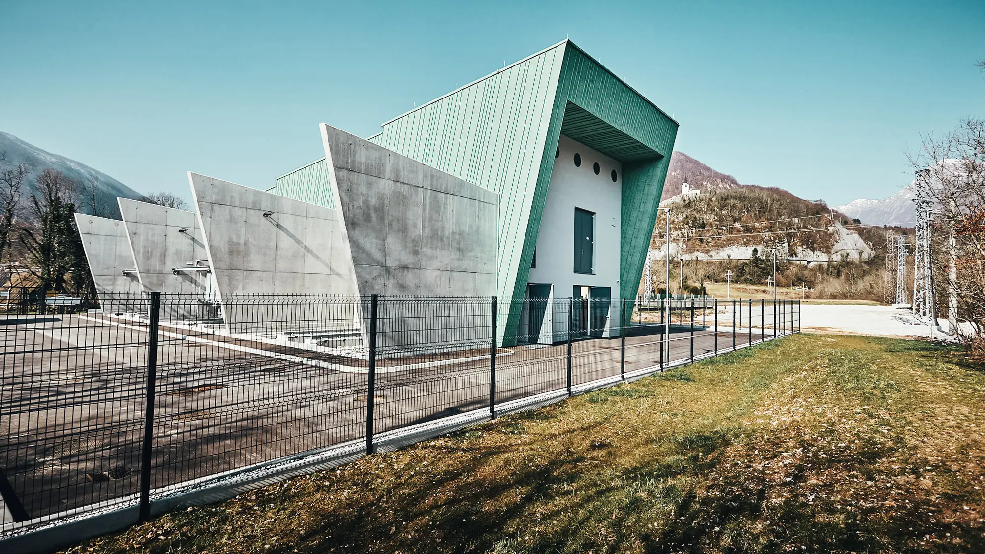 Lateral view of the substation including front and concrete partitions, fenced and with mountains in the background.