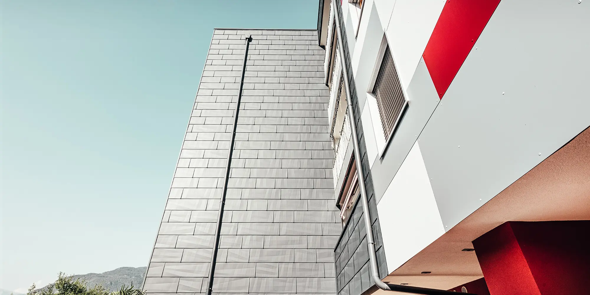 Close-up from below. In the front: the anthracite-coloured PREFA façade. Right: the white, grey and red façade front.