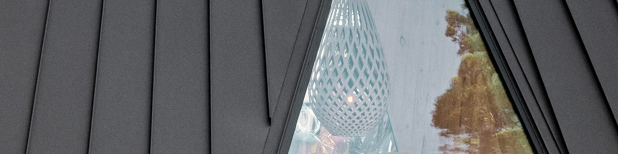 Close-up of the hut with the even PREFA aluminium and the permeable, drop-shaped lampshade that you can see through the window.