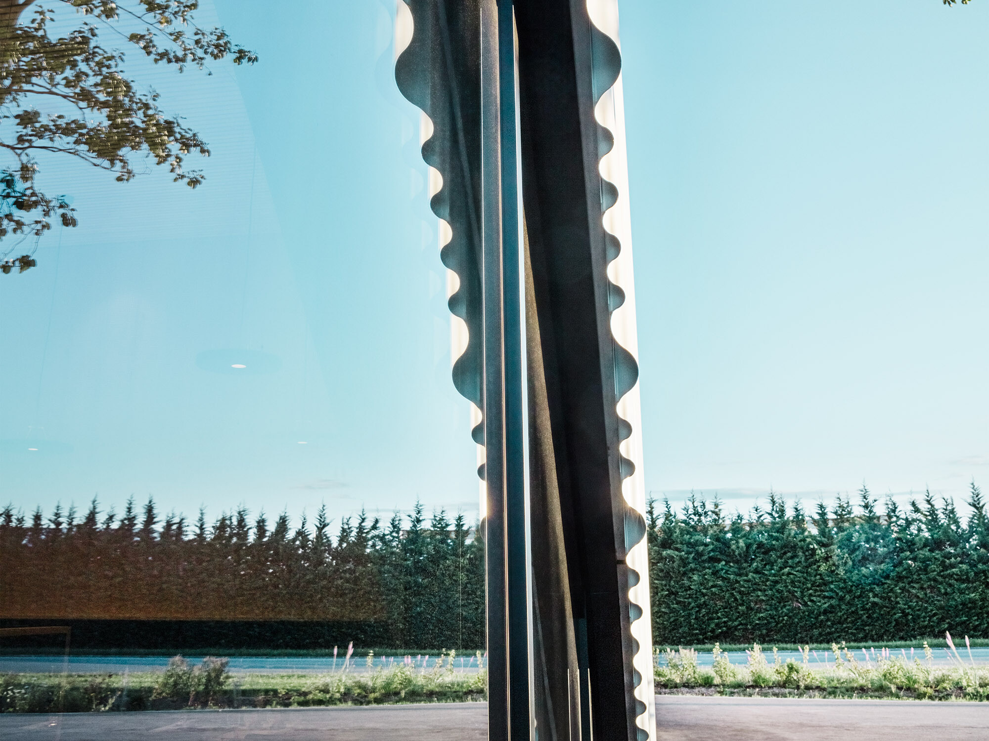 A section of the Walters restaurant showing part of a round arched window and the ends of the wavy facade. The trees in its surroundings are reflected in the glazing.