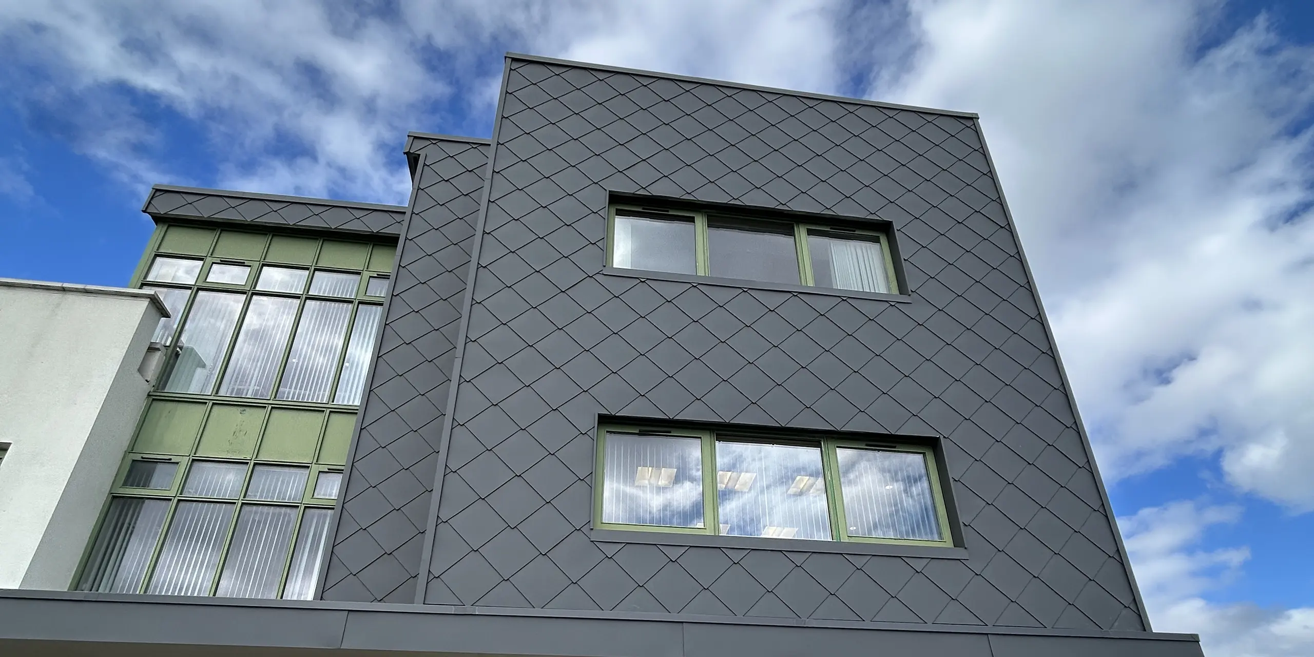 Die moderne Gebäudefassade des CAHMS Centres in Wexford wurde mit PREFA Wandraute 44 x 44 in der Farbe P.10 Dunkelgrau verkleidet. Die markante Rautenstruktur erzeugt lebendige Licht- und Schatteneffekte, während die grün gerahmten Fenster frische Kontraste setzen. Die langlebige Aluminiumfassade überzeugt durch ihre hohe Witterungsbeständigkeit, ihren Korrosionsschutz und ihren minimalen Wartungsaufwand.