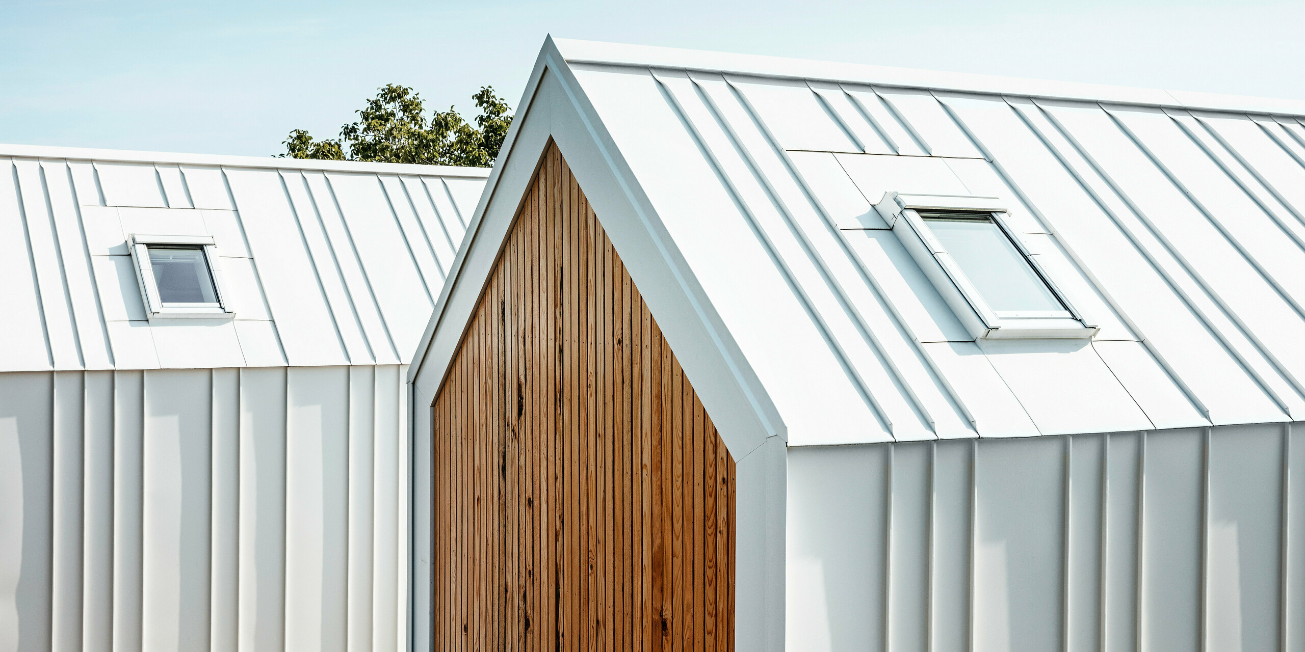 Detailed view of the white PREFALZ roof and façade cladding of the tiny houses 'Pri Momi' in Kančevci, Slovenia. The buildings are designed in a modern combination of high-quality aluminium in P.10 pure white and natural wood. The picture shows the precisely executed rebates and the elegant transition from the roof to the façade, which was realised without any visible interruption to the vertical standing seams. The harmonious choice of materials emphasises the minimalist design of the exclusive guest accommodation.