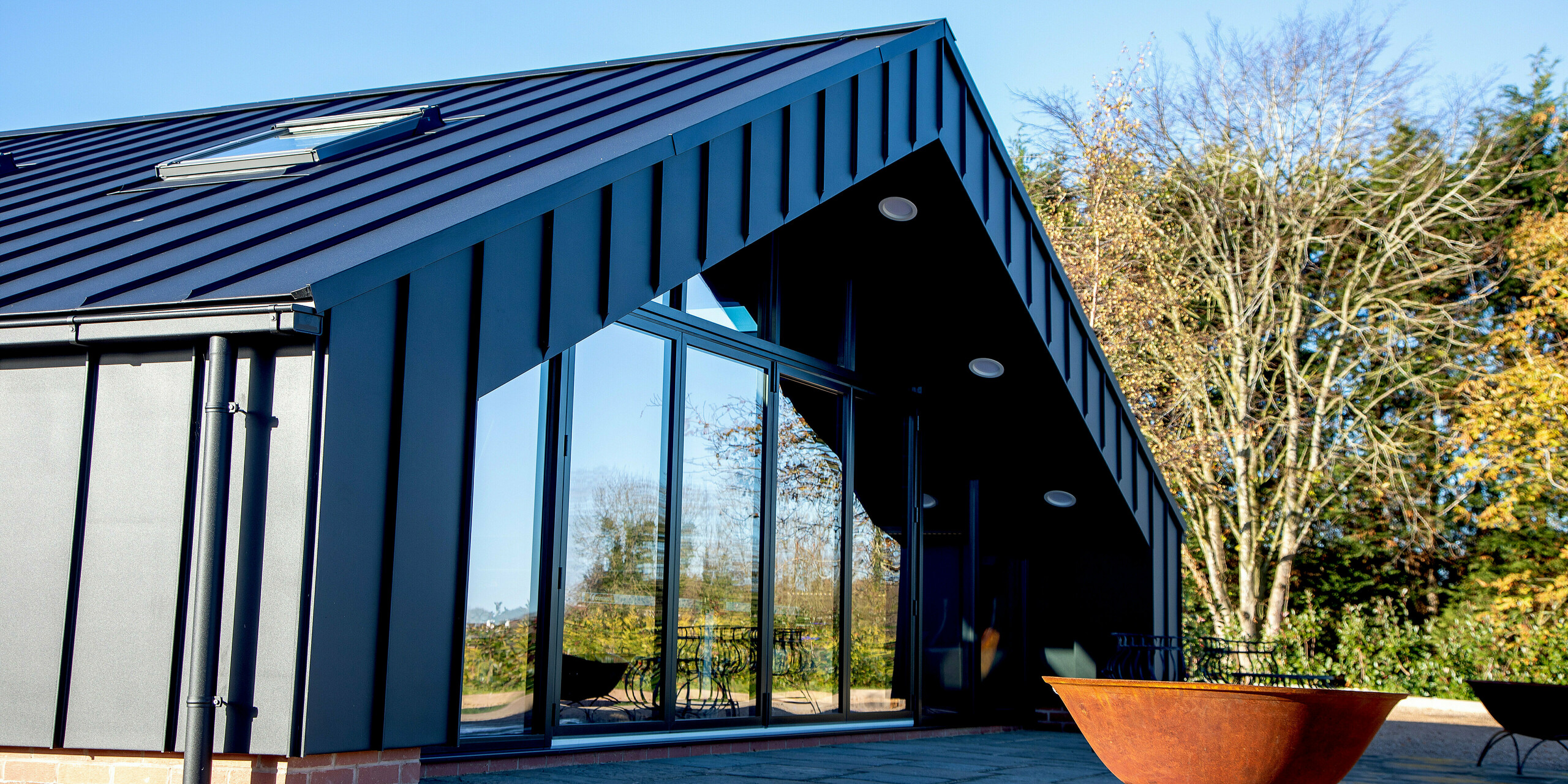 Low‑angle view of the modern leisure building clad entirely with PREFA aluminum and PREFALZ in P.10 black. The sharp standing seam lines, striking roof geometry and expansive glass façade create a bold architectural presence. The durable, weather‑resistant aluminum construction ensures long‑lasting stability and protection in outdoor environments.