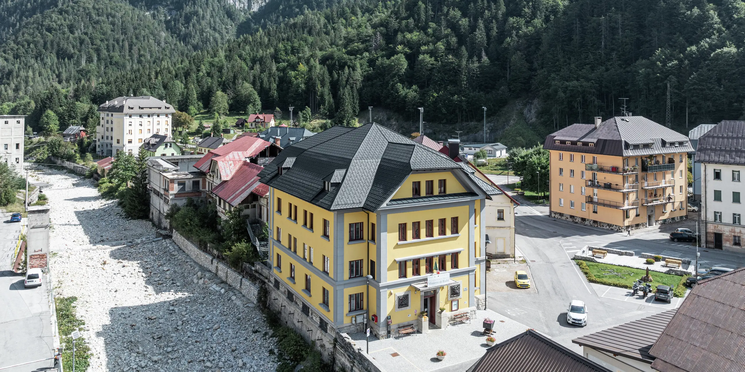 Eingebettet in eine beeindruckende Berglandschaft liegt das Museo Cave del Predil in Italien. Das Museum mit der auffallend gelben Fassade ist mit hochwertigen PREFA Dachplatten in der Farbe P.10 Anthrazit ausgestattet. Das widerstandsfähige Blechdach garantiert optimalen Schutz vor alpinen Witterungseinflüssen wie Schnee und Sturm, gepaart mit ästhetischem Design. Im Hintergrund erhebt sich majestätisch das Alpenpanorama mit dichten Wäldern und felsigen Gipfeln.