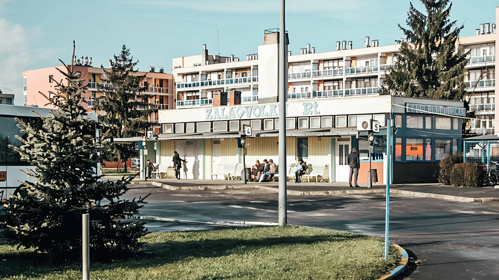 A picture of the old railway station in Lenti. People are sitting on a bench in the sun waiting for the bus.