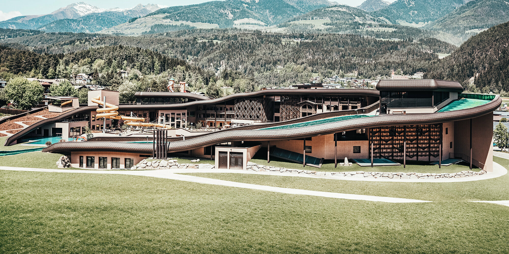 View of the entire hotel complex from a distance: The roof wave runs across the entire building with a beautiful  hilly, wooded landscape in the background