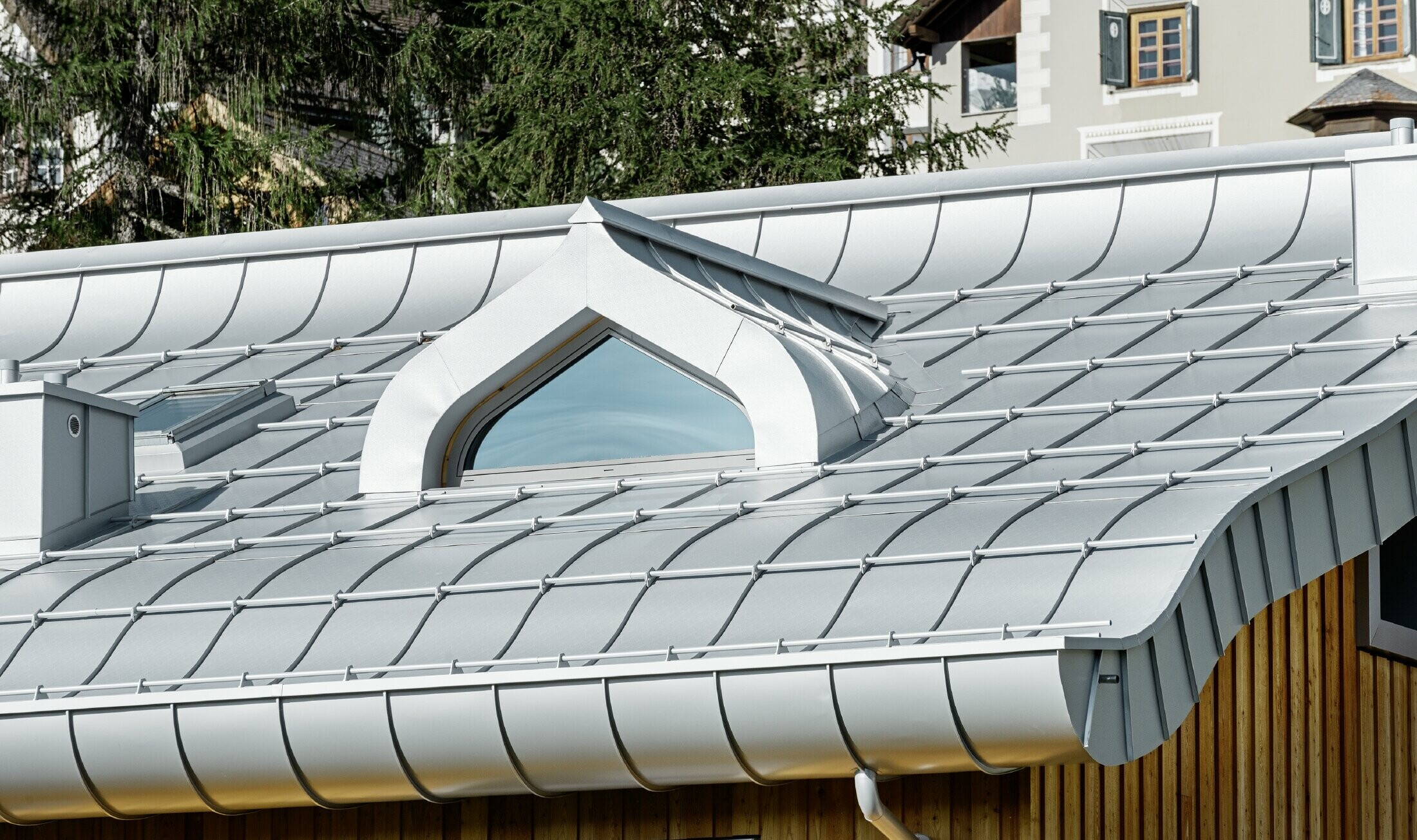 Residential complex in St. Moritz (Switzerland) with a wooden façade and an aluminium roof with undulating eaves in metallic silver