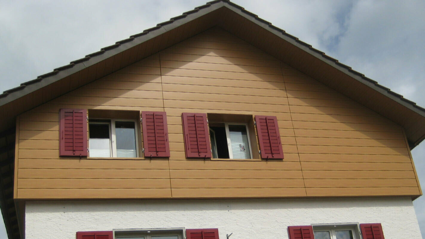 House façade with wood-effect PREFA sidings, installed horizontally; windows with red shutters