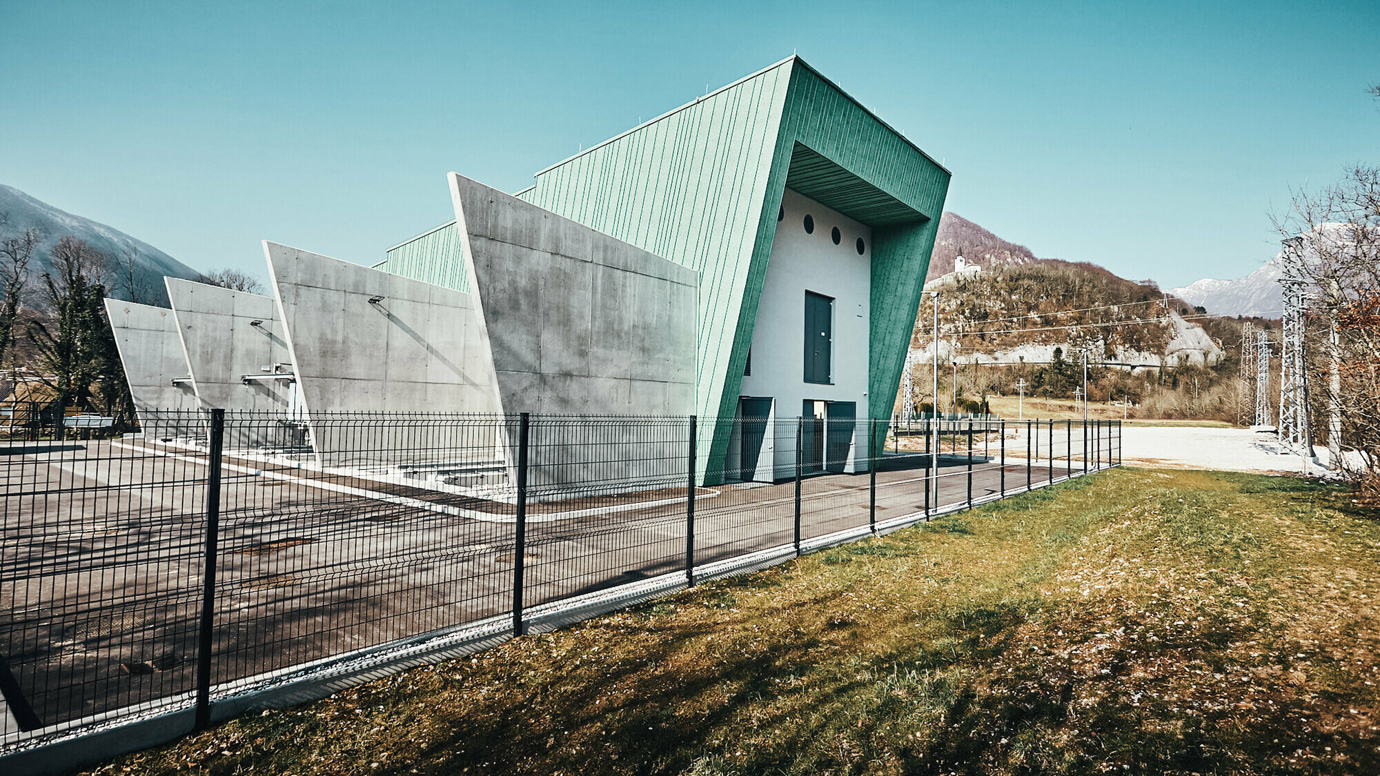 Lateral view of the substation including front and concrete partitions, fenced and with mountains in the background.