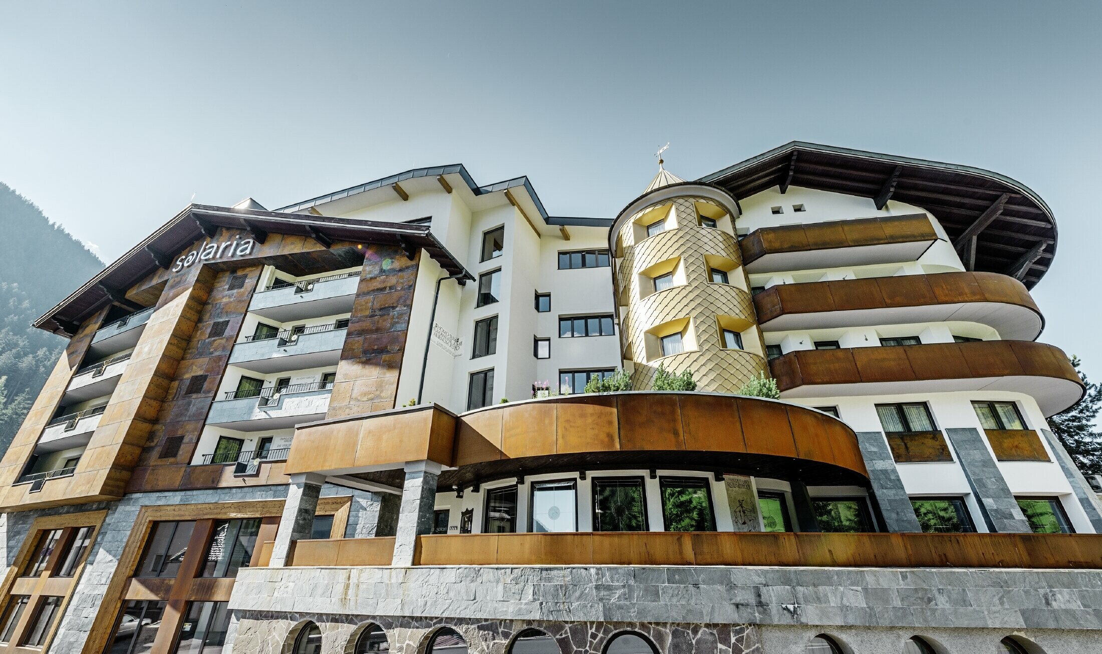 Traditional hotel in Ischgl (Austria) with wooden balconies, a wooden façade and tower clad in PREFA gold-coloured aluminium panels