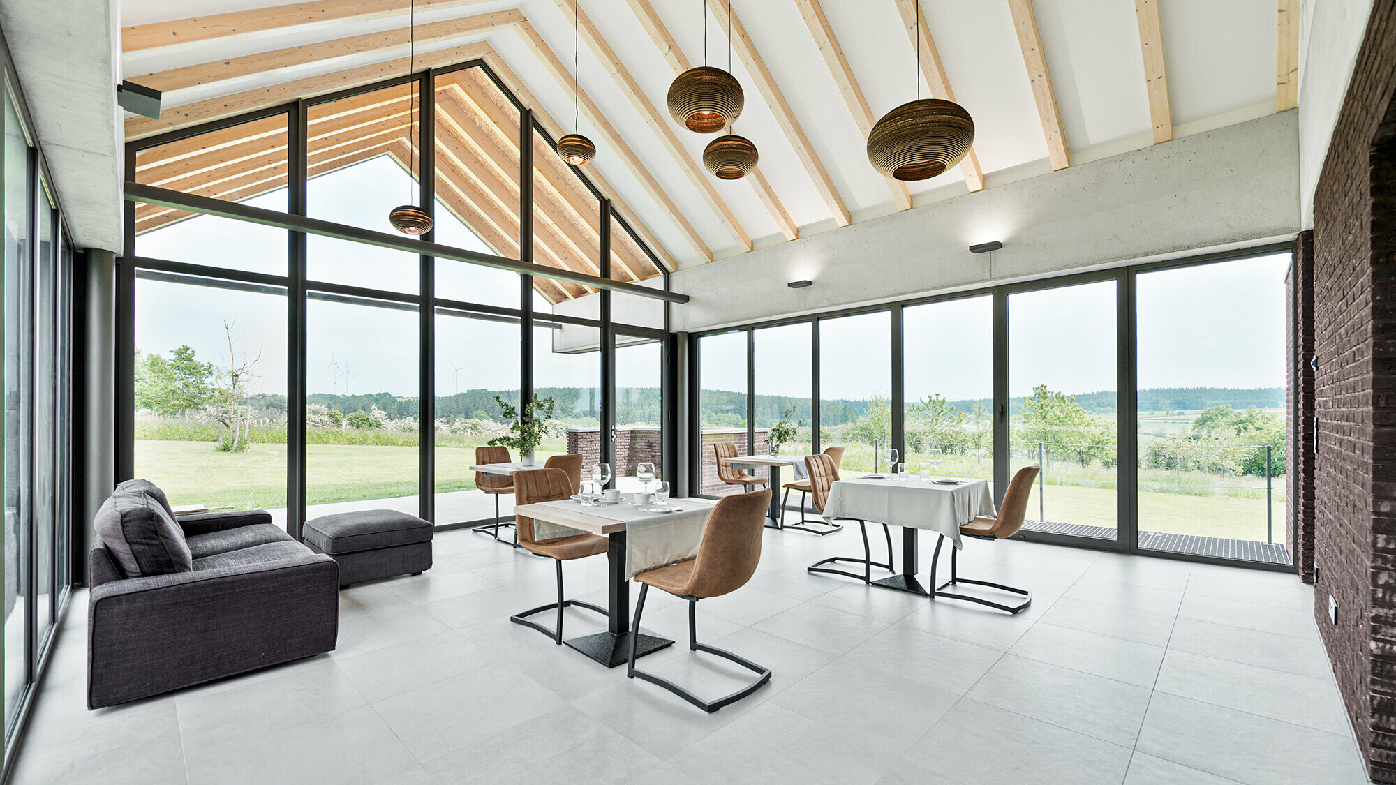 Interior view of the dining room in harmonious earth and beige tones. The generous glazing ernables a sweeping view of the Warche valley and the garden belonging to the owners of the accommodation.