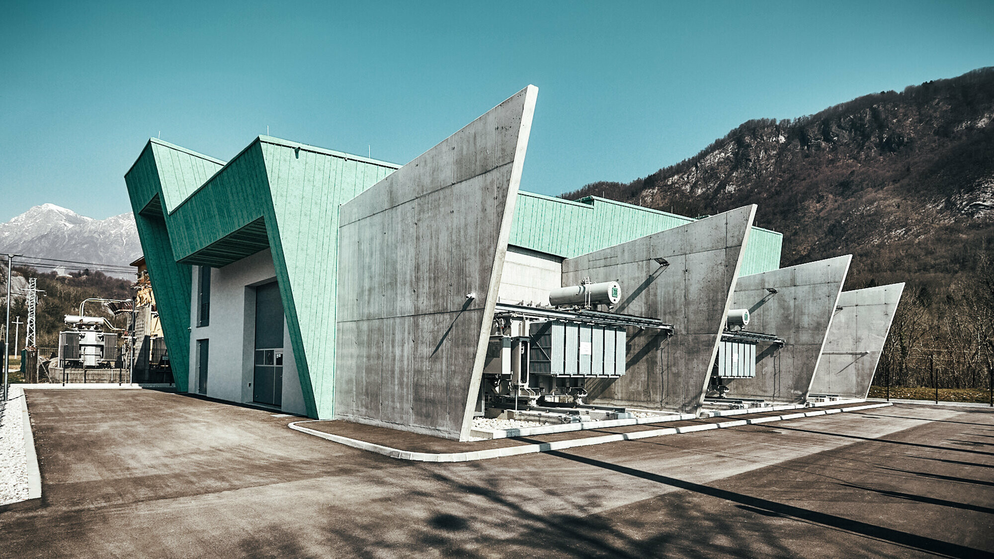 Lateral view of the substation including front and concrete partitions, fenced and with mountains in the background.