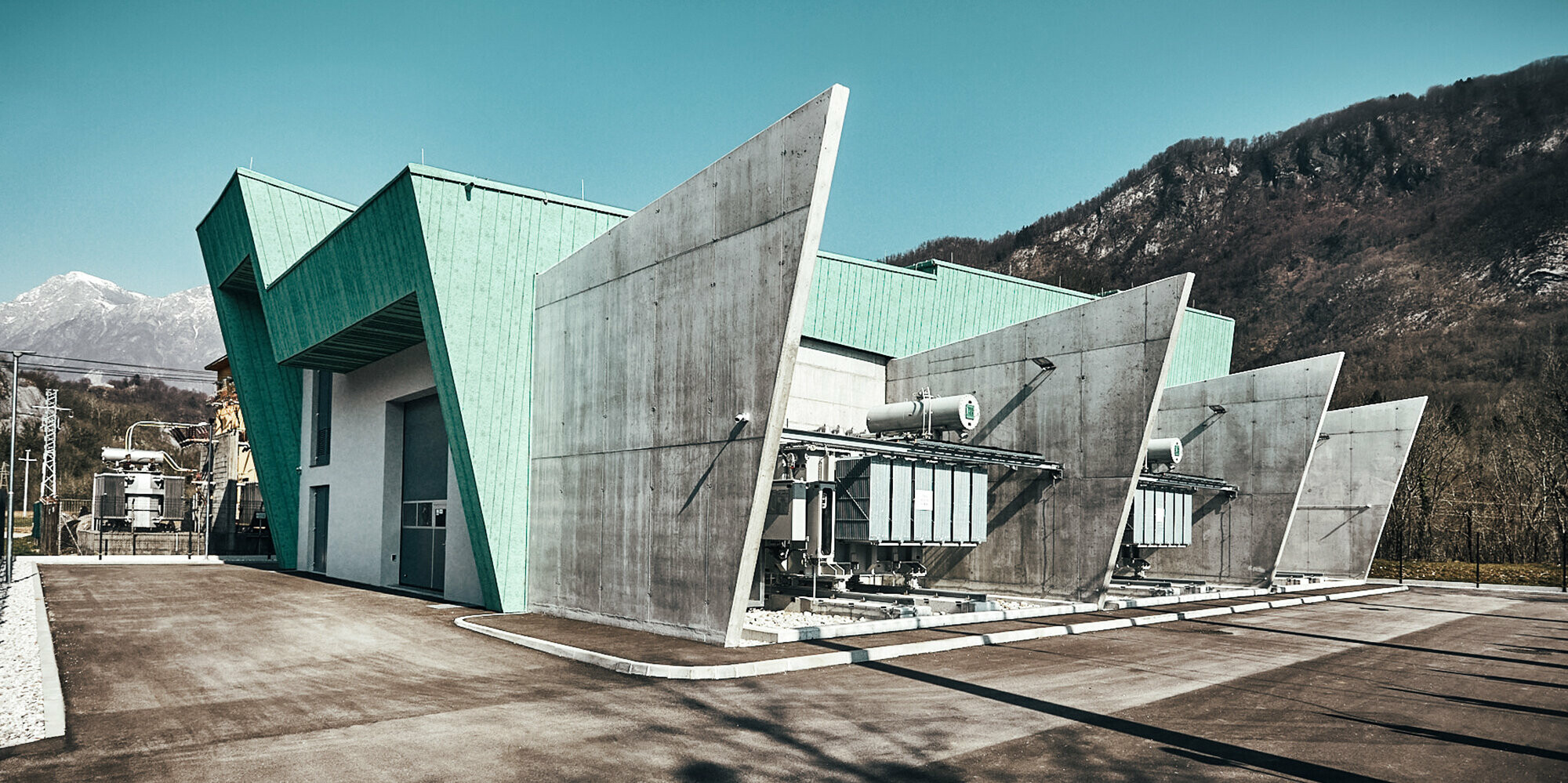 Lateral view of the substation including front and concrete partitions, fenced and with mountains in the background.