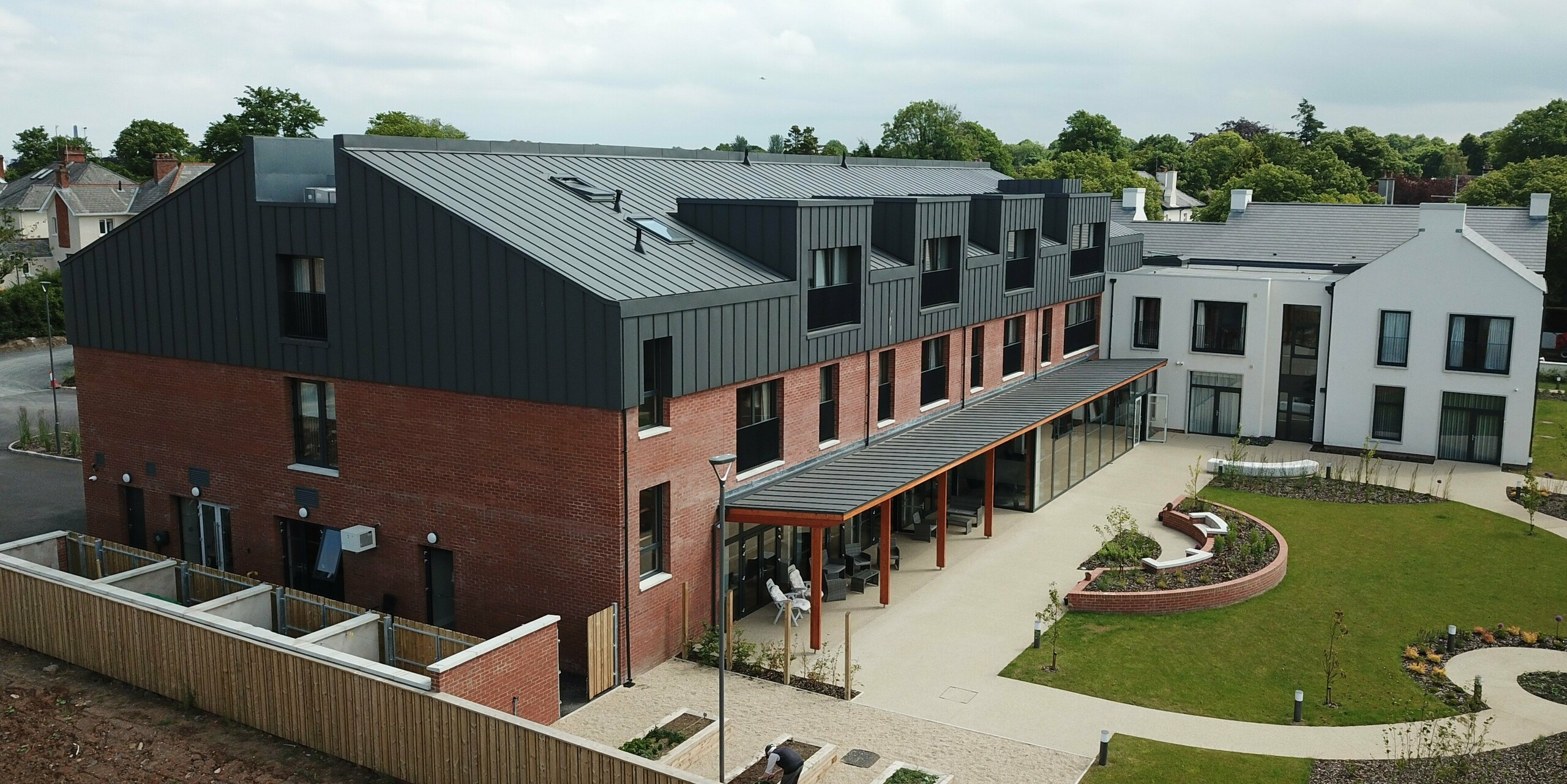 Side view of Harberton Hall with clinker brick façade and PREFALZ aluminium cladding in P.10 dark grey. The flat roof dormers and the modern mix of materials create a timeless appearance. The building for assisted living combines sustainability, functionality and elegant design.