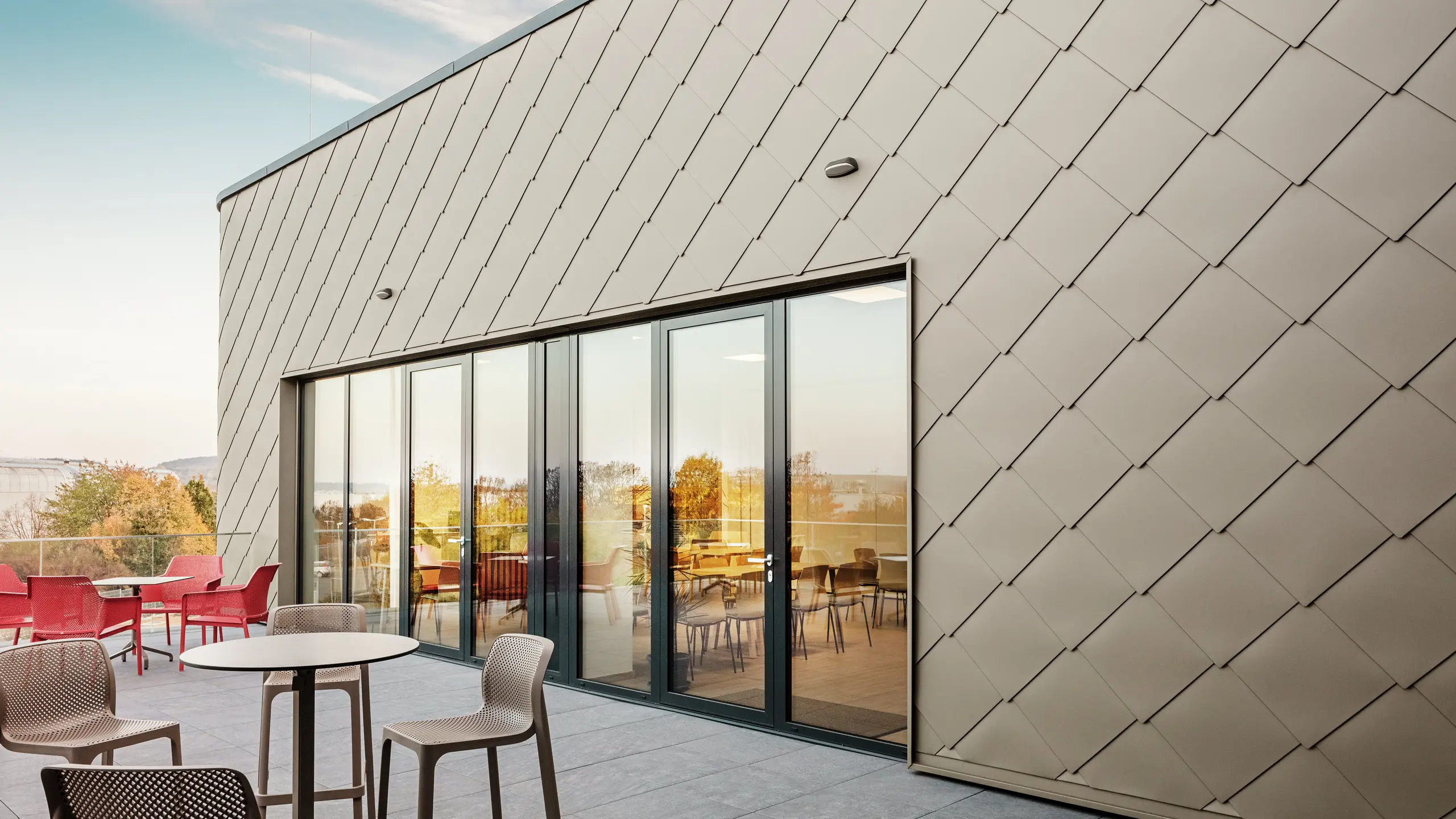 The façade of the new PREFA site in Törökbálint impresses with its elegant PREFA rhomboid façade tiles 44 × 44 in P.10 Prefabronze. The precisely installed aluminium façade ensures a modern, dynamic appearance while offering maximum protection against the elements. The generous glass front connects the internal and external areas and creates a bright and inviting atmosphere on the spacious terrace.