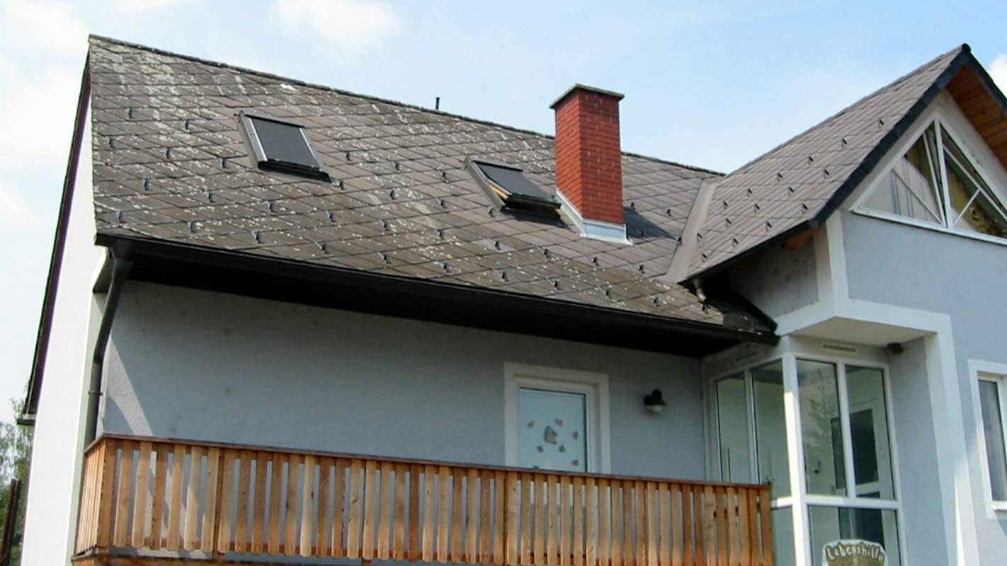 Detached house with a gable roof, blue façade and brick chimney with an old roof ready for renovation