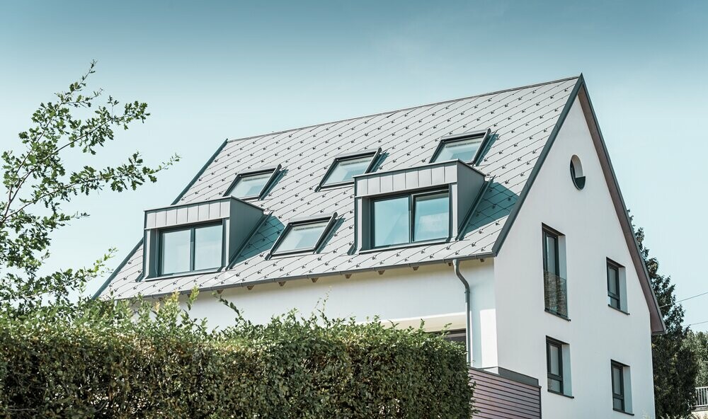 Roof refurbishment of a gabled roof with two dormers and four roof windows. The roof was covered with PREFA light grey 44 × 44 rhomboid roof tiles. The PREFA hanging gutter, also in light grey, was used for the guttering. 