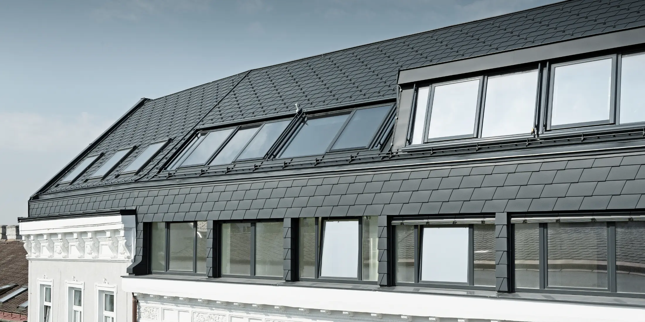 Extended roof conversion of a residential complex in Mariahilferstraße, Vienna; covered with PREFA roof shingles and façade shingles in anthracite P.10.