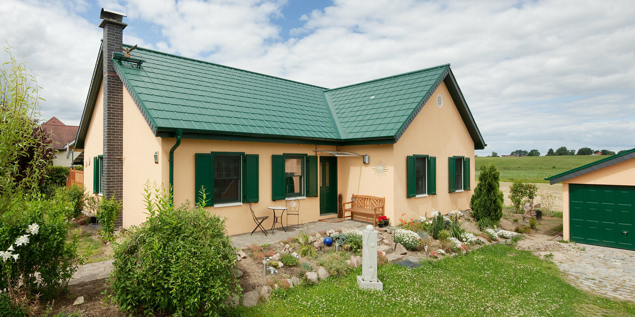 Extended gable roof; L-shaped gable roof; with PREFA roof tiles in P.10 moss green; pretty rural cottage with green shutters to match the PREFA roof.