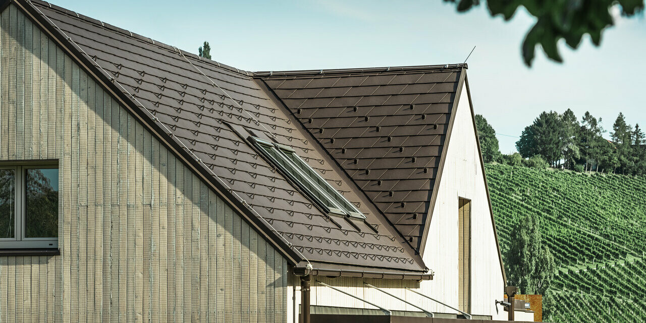Detached house with two gable roofs was covered with PREFA roof shingle in nut brown. The roof drainage is performed via the PREFA box gutter. The façade is clad with weathered wood.