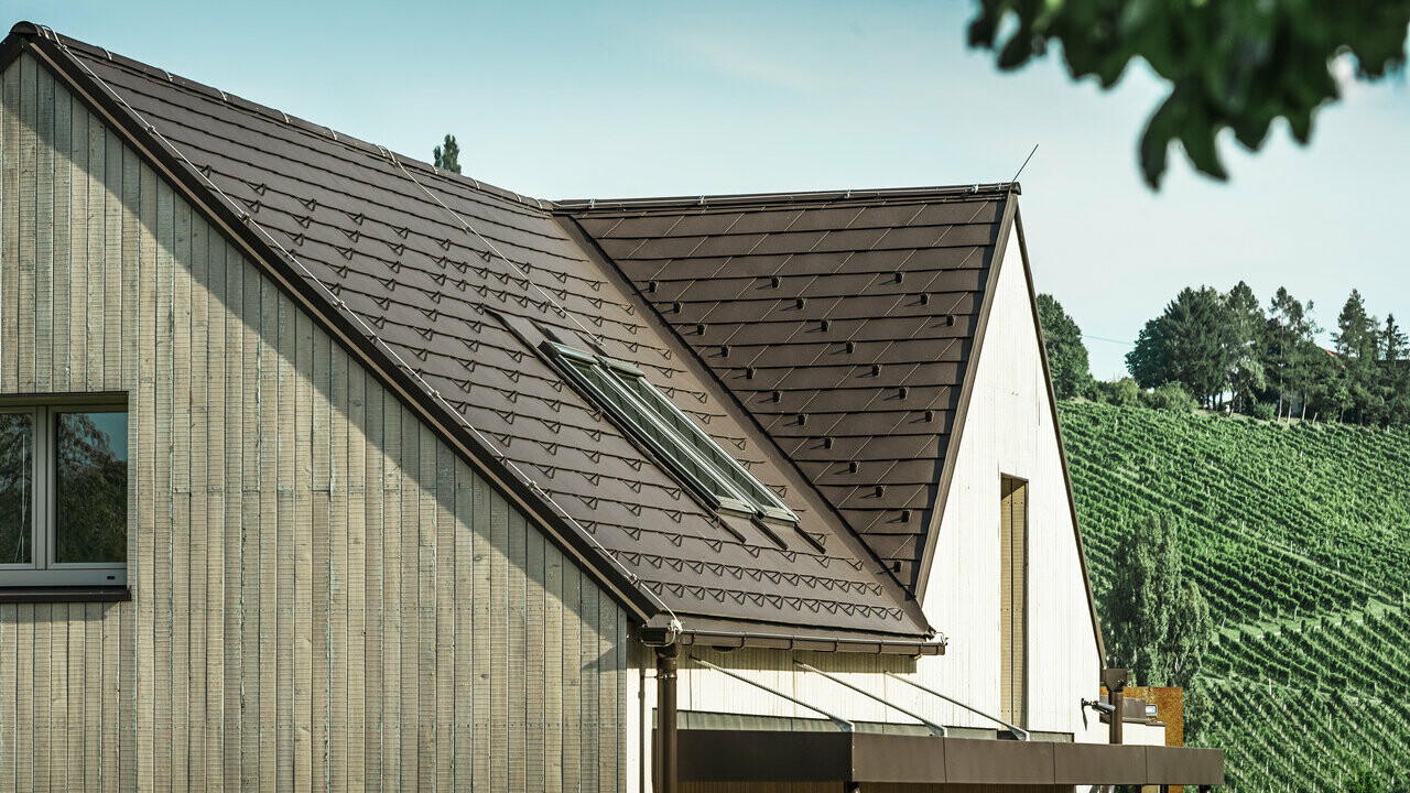 Detached house with two gable roofs was covered with PREFA roof shingle in nut brown. The roof drainage is performed via the PREFA box gutter. The façade is clad with weathered wood.