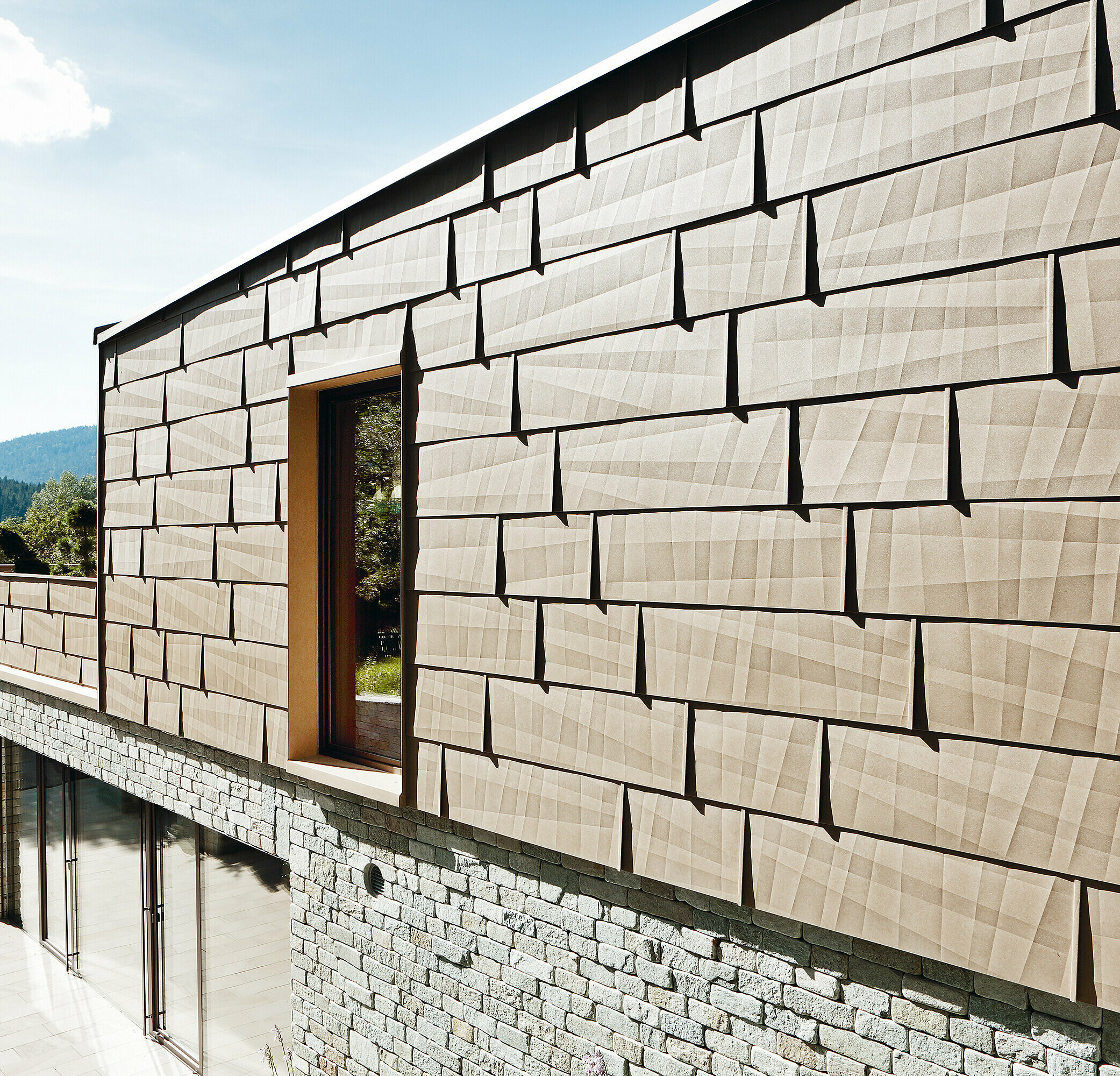On this external façade, the PREFA FX.12 façade panel in P.10 sand brown has been combined with a stone façade on the bottom floor.