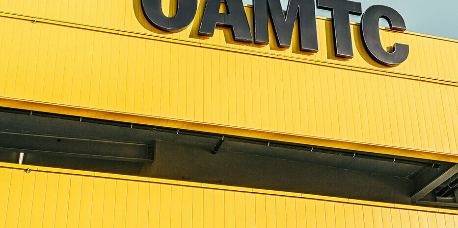 Close-up of the ÖAMTC Logo. The façade is covered in PREFA Sidinds in the bespoke colour rapeseed yellow and slate grey.