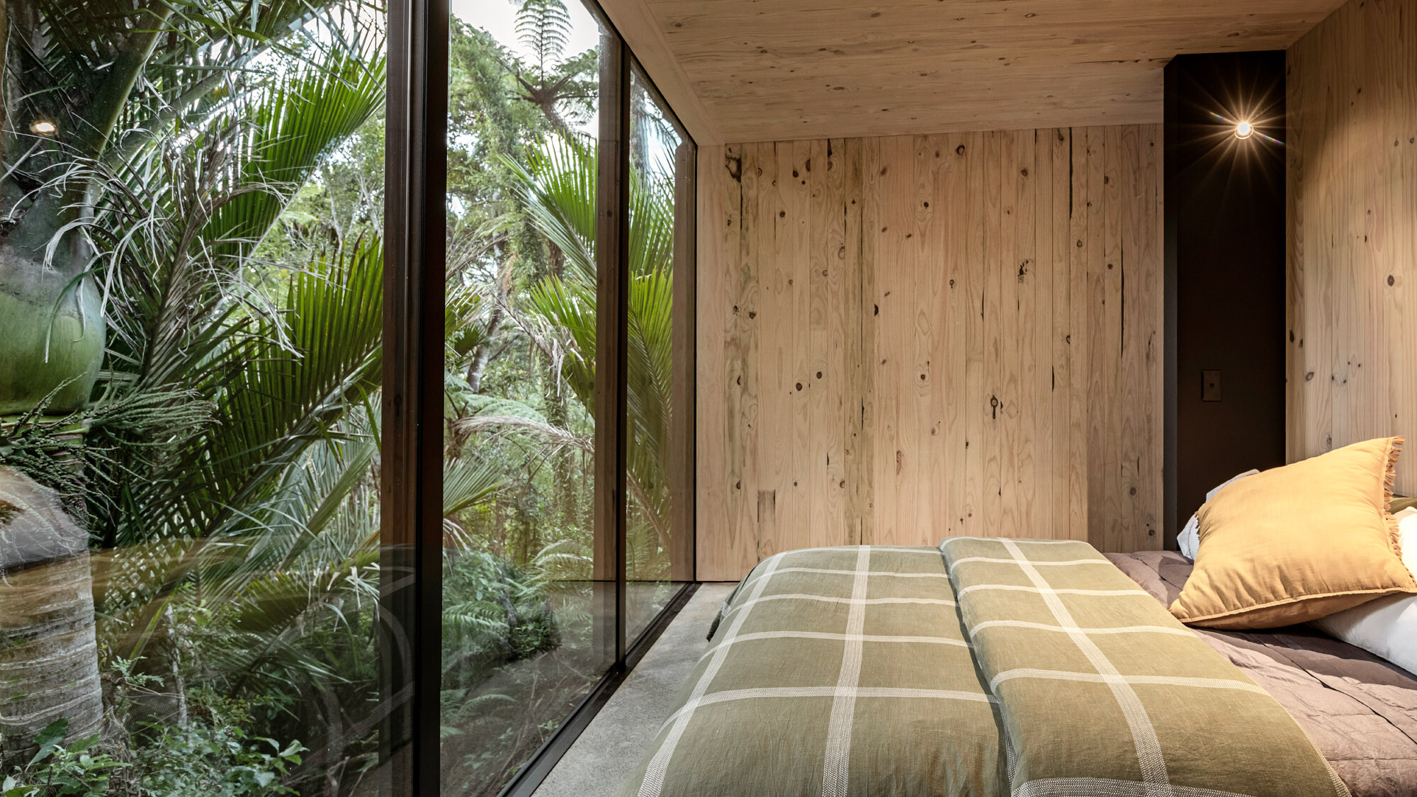 The bedroom with the floor-to-ceiling window, the bush borders directly behind it.