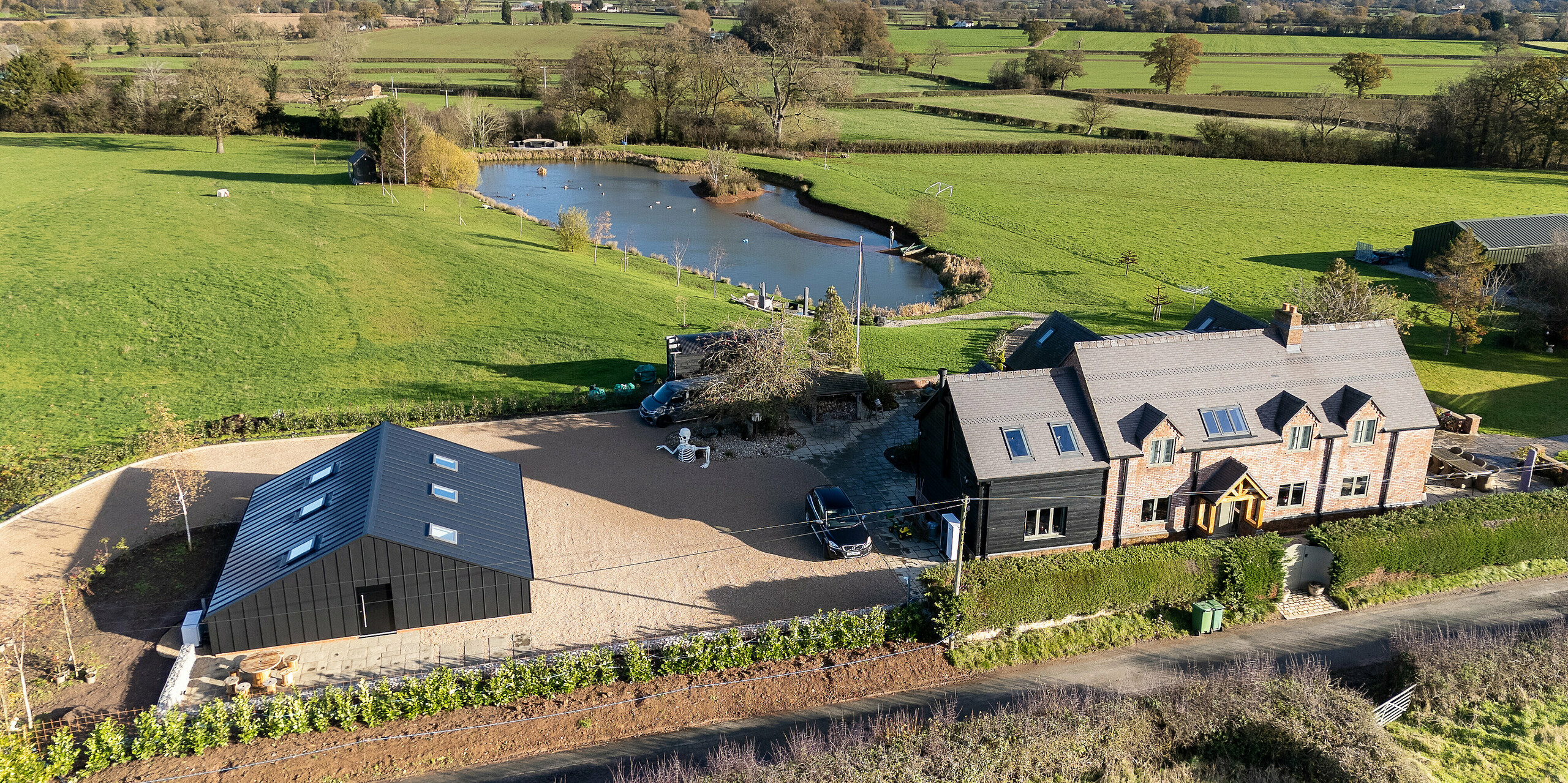 Aerial view of the modern leisure building featuring a complete PREFA aluminum façade and PREFALZ standing seam roofing in P.10 black. The clean geometric architecture contrasts with the expansive rural landscape. The durable, weather‑resistant aluminum envelope ensures long‑lasting protection and highlights the premium design within the large countryside property.